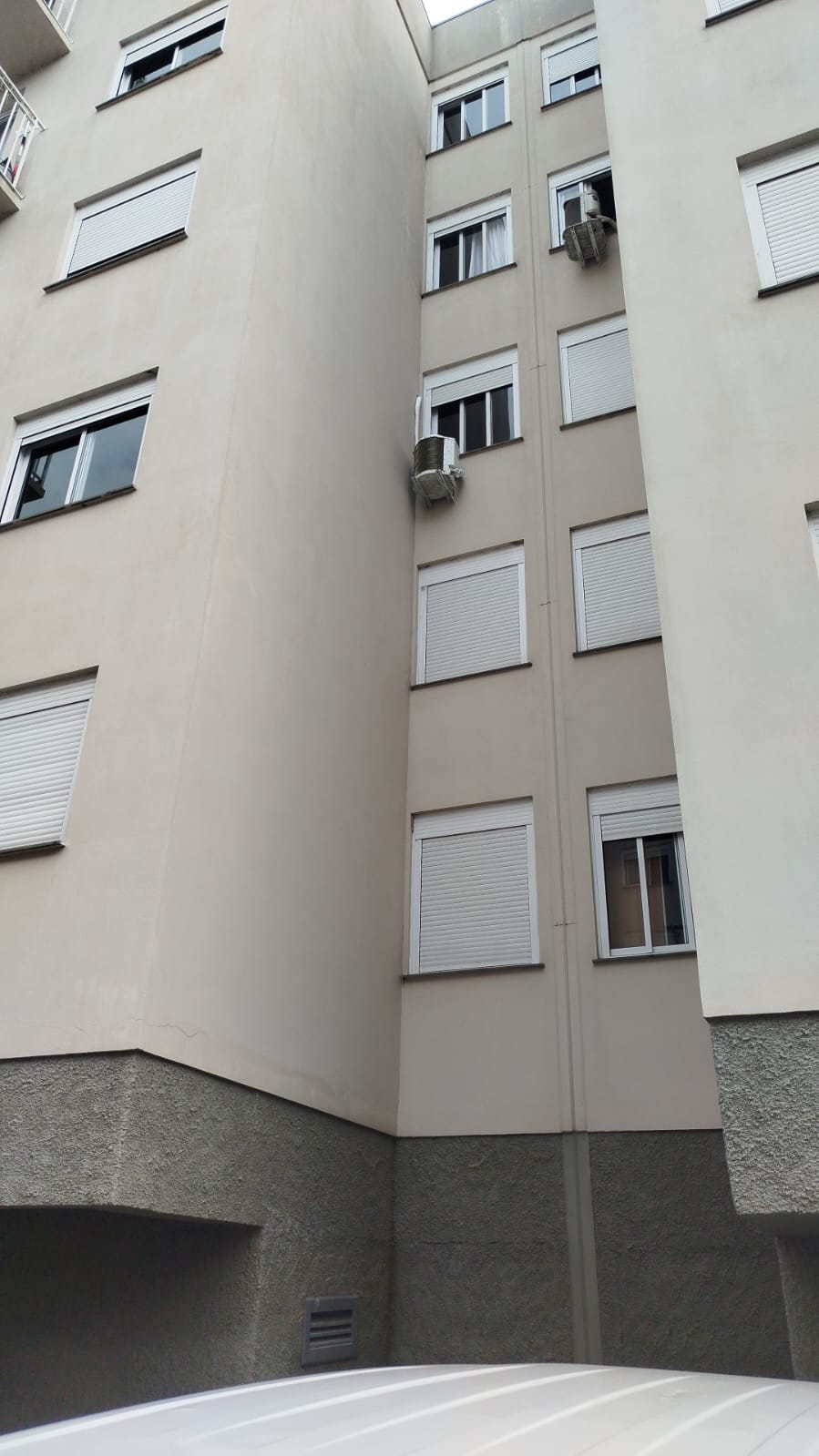 fachada de prédio residencial bege vista de baixo, com janelas de persianas brancas e aparelhos de ar-condicionado  — te